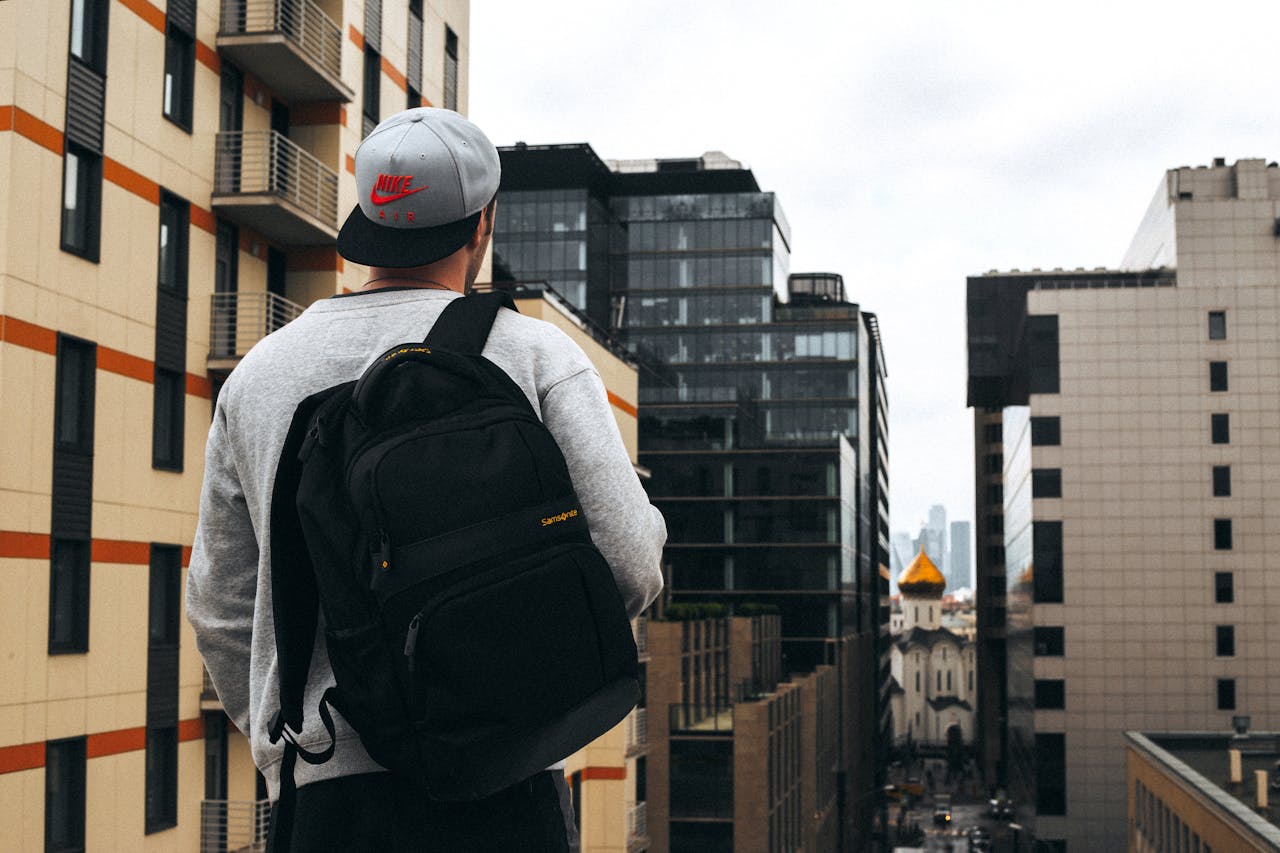 Man with backpack and cap stands on a Moscow street surrounded by modern buildings.