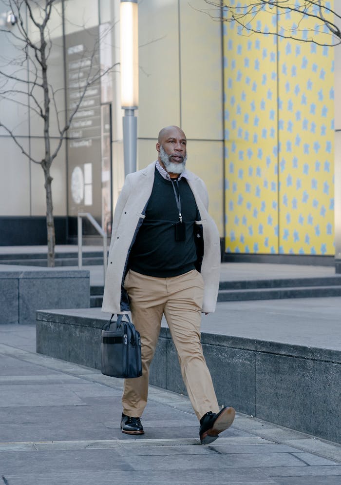 A mature man in a suit confidently walks down a city street, holding a bag.